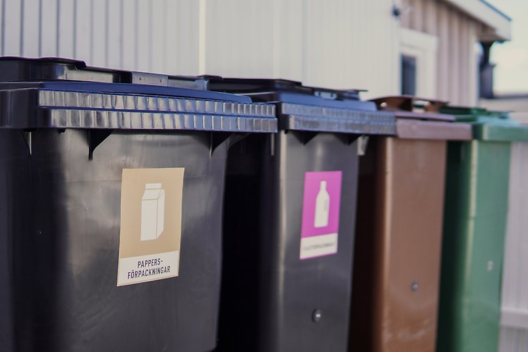 Fyra soptunnor bredvid varandra, en brun för matavfall, en grön för restavfall, en svart för plastförpackningar och en svart för pappersförpackningar, illustration.