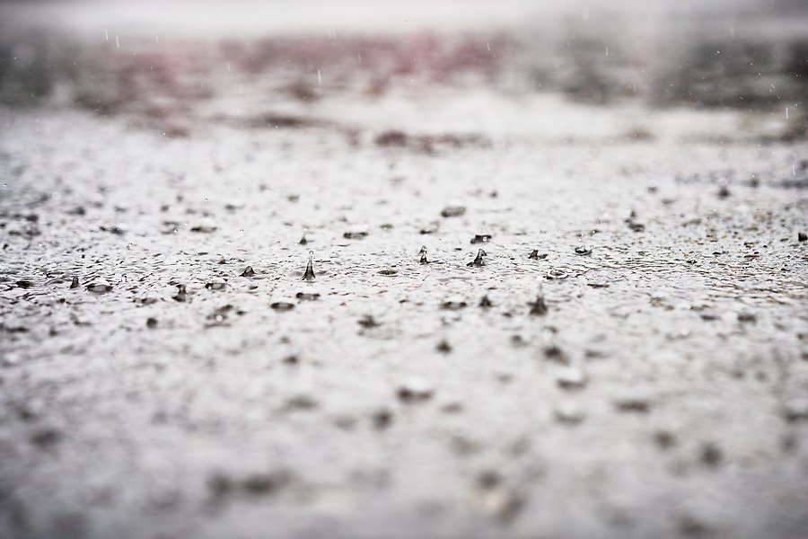 På ojämn blanksvart asfalt studsar regndroppar, foto.